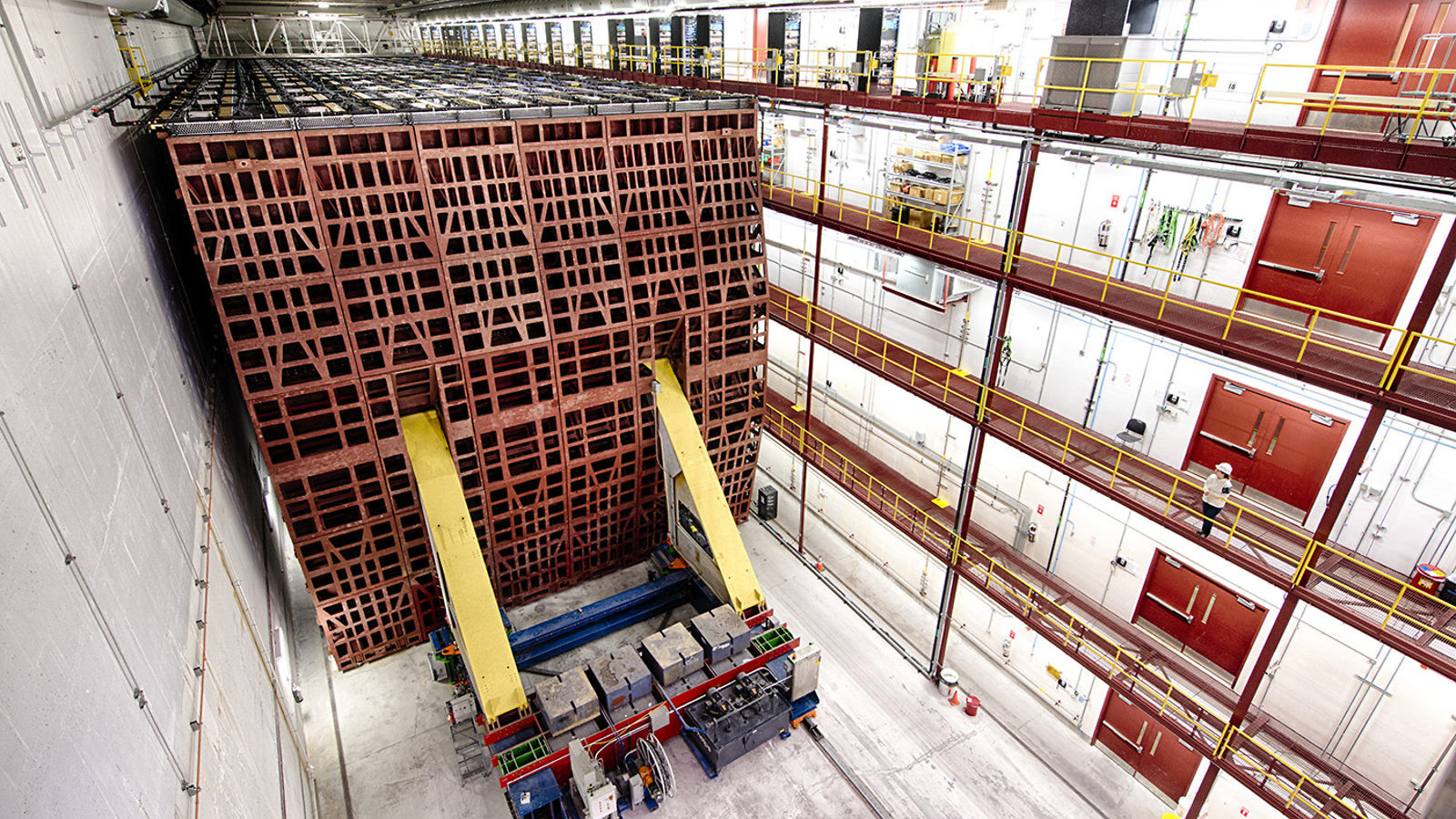 High view of a large white chamber, five stories tall with railed gangways along the far wall, containing the large cubic structure with latticed surface and attached scientific equipment that forms the Far Detector of the NOvA Experiment